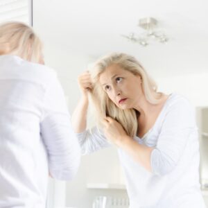 Senior beautiful woman standing in front of mirror looking in her hair.
