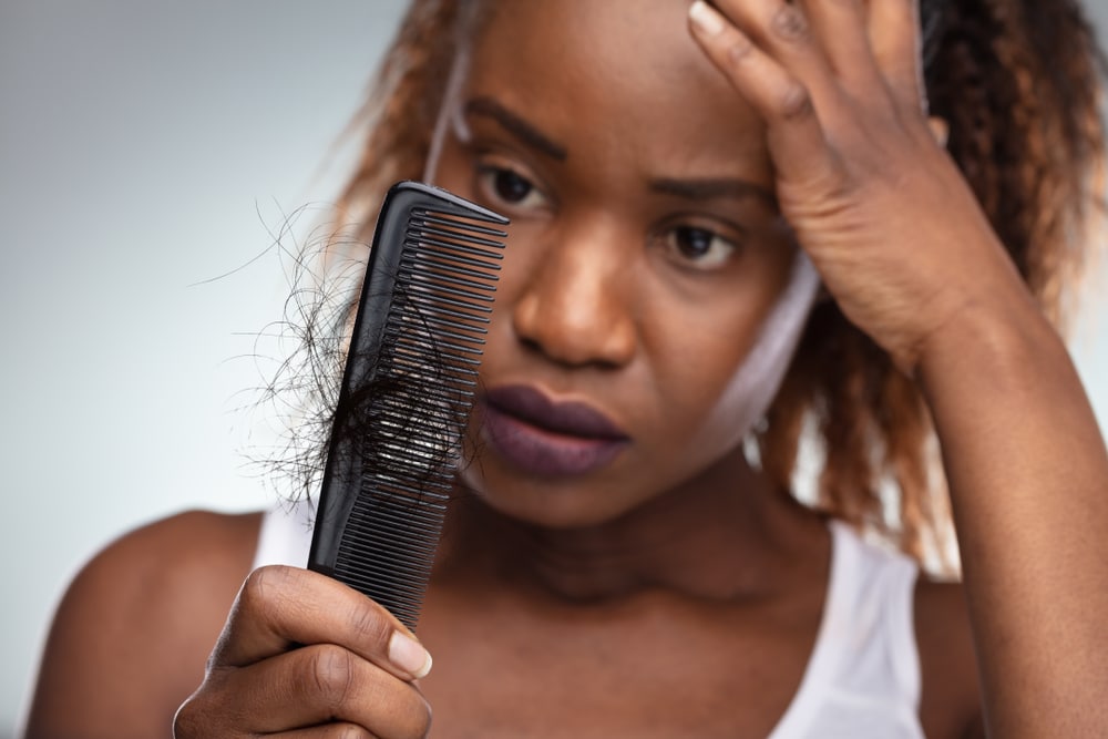 Woman unhappy as she looks at a comb with her hair falling out needing hair loss treatment.